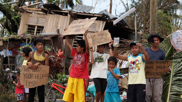 Crianças erguem cartazes pedindo ajuda e comida à beira de uma rodovia em Tabogon, na província de Cebu, atingida pelo tufão