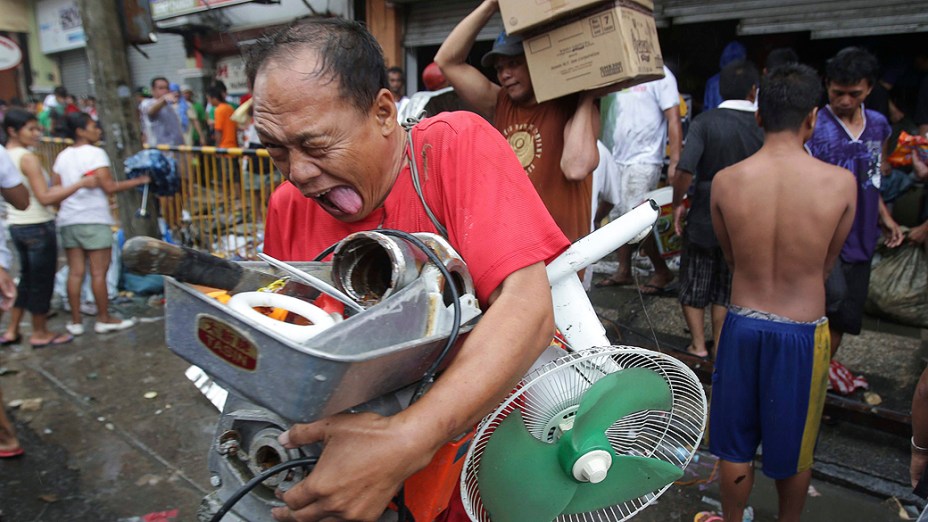 Homem leva suprimentos de loja invadida na cidade de Tacloban, nas Filipinas