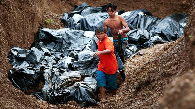 Filipinos ajudam a mover os corpos para o enterro em uma vala comum de vítimas do tufão Haiyan na cidade de Tacloban