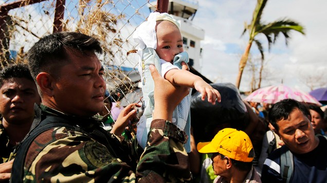 Soldado filipino segura um bebê enquanto passa pelas pessoas no aeroporto de Tacloban