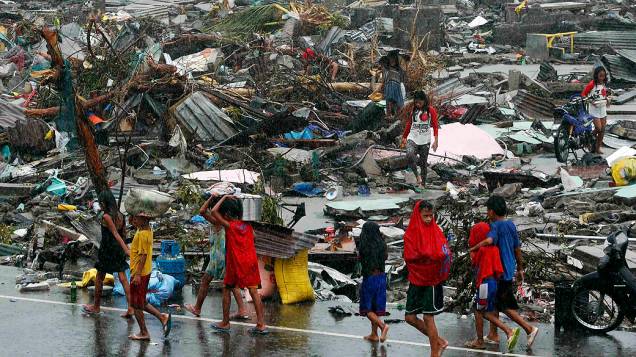Sobreviventes carregam seus pertences entre casas destruídas pela passagem do supertufão Haiyan na cidade de Tacloban, na região central das Filipinas