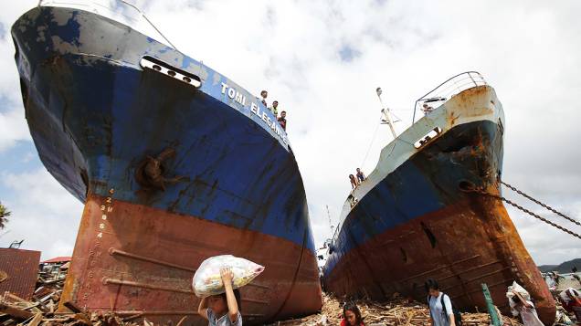 Sobreviventes passam por dois grandes barcos que foram arrastados por fortes ondas causadas pelo supertufão Haiyan na cidade de Tacloban, nas Filipinas