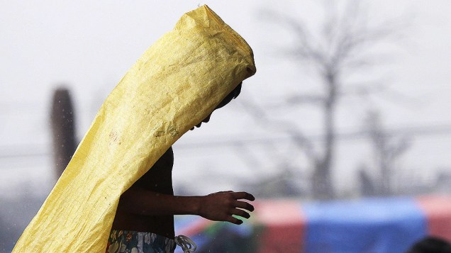 Menino cobre a cabeça enquanto caminha na chuva pelas ruas de Tacloban, na ilha de Leyte, Filipinas. Milhares de sobreviventes sofrem escassez de alimentos e água após a passagem do supertufão "Haiyan" na última sexta-feira (07)
