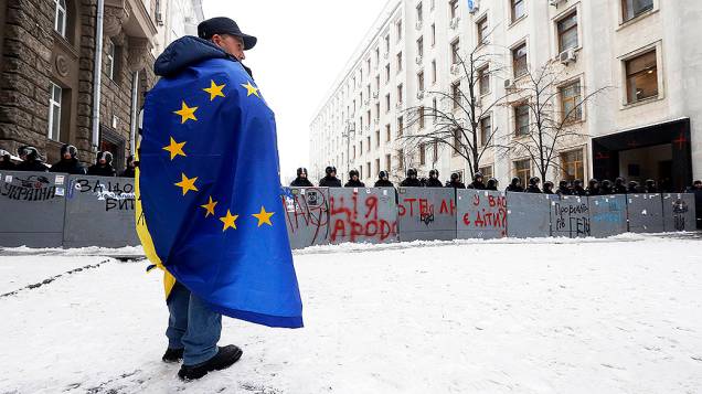 Manifestante com uma bandeira da União Européia nos ombros fica na frente de um bloqueio policial no centro de Kiev, na Ucrânia