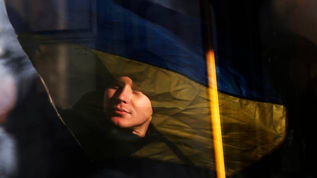 A bandeira ucraniana segurada por manifestantes é refletida no rosto de um policial que faz a segurança do prédio do governo em Kiev