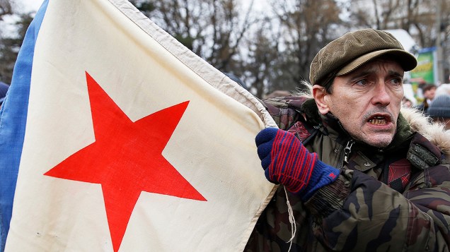 Homem segura uma bandeira militar da era soviética durante um comício pró-Rússia em Simferopol, na região da Crimeia