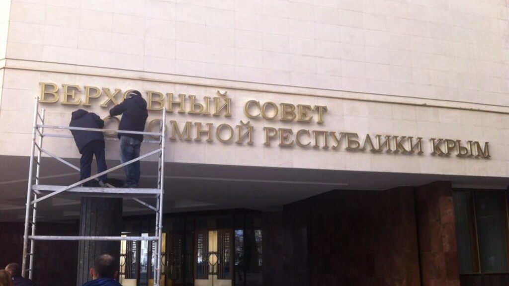 Homens tiram o letreiro que dá nome ao Parlamento da Crimeia