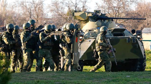 Soldados supostamente russos, se protegem atrás de um blindado, enquanto tentam invadir a base aérea de Belbek, na Crimeia