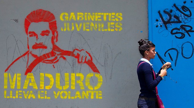 Mulher passa por um mural com desenho do presidente interino Nicolás Maduro "ao volante", em Caracas