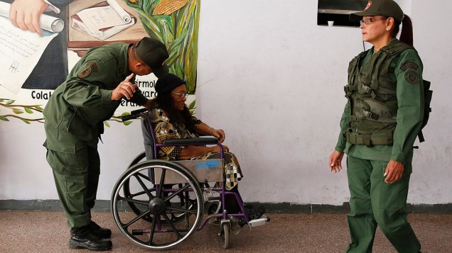 Soldado auxilia uma mulher idosa em uma cadeira de rodas em um posto de votação durante as eleições municipais em Caracas