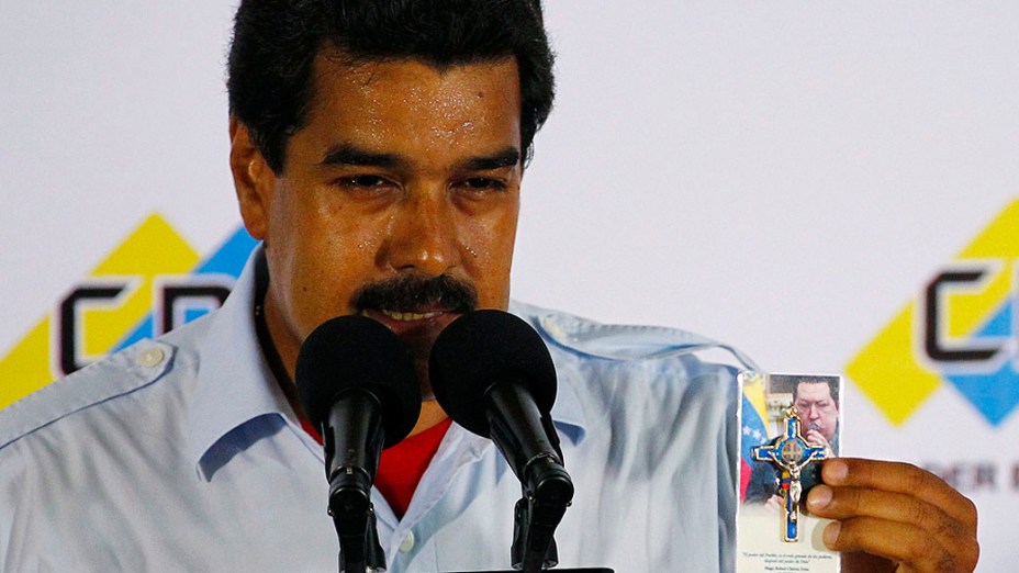 Nicolas Maduro segura lembrança religiosa com uma imagem do falecido presidente Hugo Chávez durante coletiva de imprensa no comitê eleitoral em Caracas neste domingo (14)