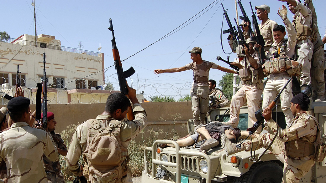 Membros das forças de segurança iraquianas celebrar perto dos corpos de militantes do Estado Islâmico do Iraque e do Levante (ISIL), que foram mortos durante confrontos, nos arredores da cidade de Samarra