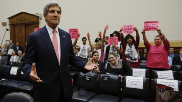 O secretário de Estado americano John Kerry participa de audiência no Congresso sobre intervenção na Síria. Ao fundo, manifestantes contrários a ação militar