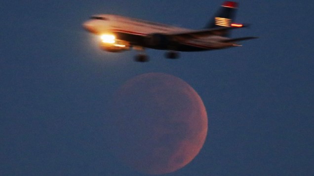 Avião comercial passa acima da Lua de sangue no aeroporto Nacional Ronald Reagan em Washington DC. Fenômeno do eclipse lunar dá tom avermelhado à Lua