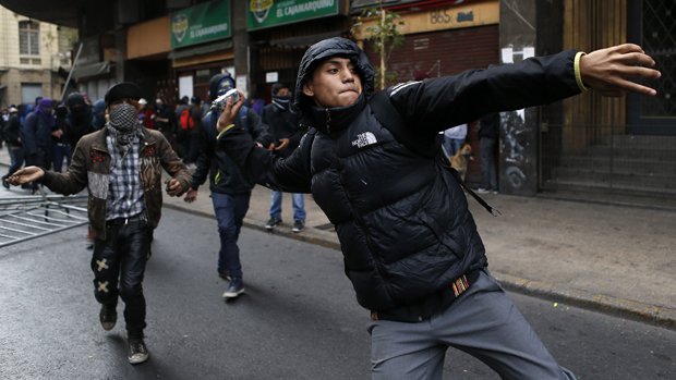 Estudante atira pedra em policiais durante manifestação em Santiago, no Chile