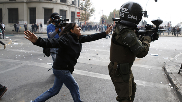 Mulher tenta impedir policial de atirar contra estudantes em protesto na capital chilena