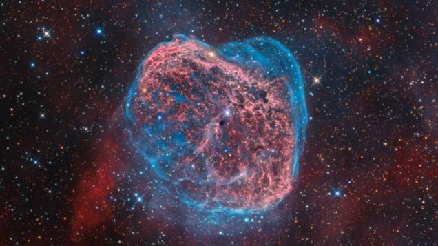 <p>Coração da Nebulosa Crescente brilhando em azul e vermelho. Considerada uma nebulosa de emissão, pois rodeia uma estrela quente, ela é composta pela matéria ejetada de uma estrela poderosa e de vida curta, a Wolf-Rayet, vista no centro da imagem. Radiação ultravioleta e vento estelar aquecem a nuvem, fazendo-a brilhar</p>