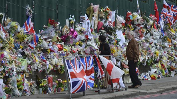 Moradores observam flores colocadas no local onde o soldado britânico Lee Rigby foi destroçado por dois terroristas islâmicos no dia 22 de abril, em Woolwich, sudoeste de Londres