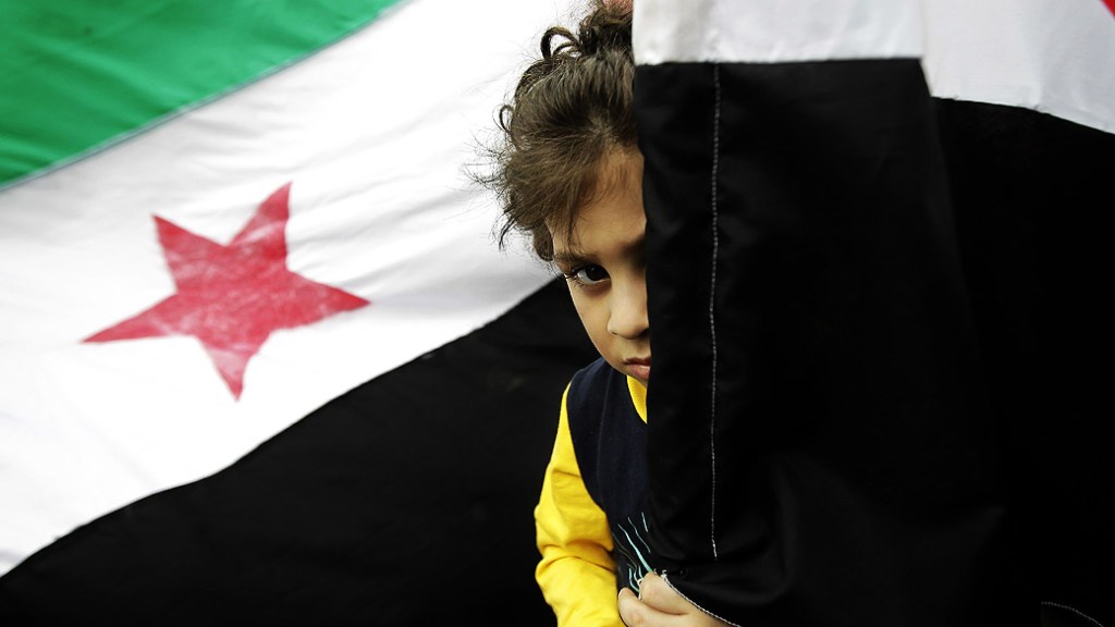 Criança síria se esconde atrás de bandeira, no Líbano