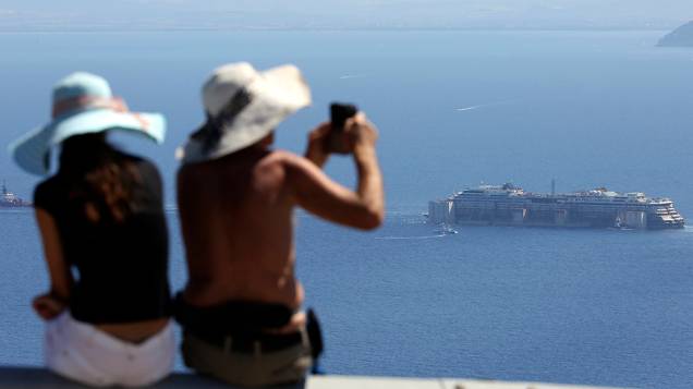 Turistas fotografam os restos do navio naufragado Costa Concordia, próximo a Ilha de Giglio, região central da Itália