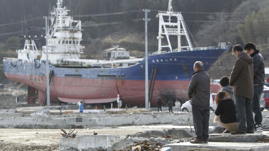 Família faz orações diante do navio Kyotoku Maru No. 18, encalhado em Kesennuma desde o tsunami de 2011
