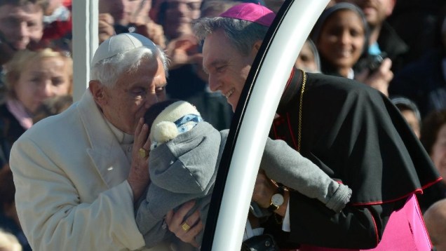 O papa Bento XVI beija uma criança observado por seu secretário, Georg Gaenswein, na Praça de São Pedro, no dia de sua última audiência pública