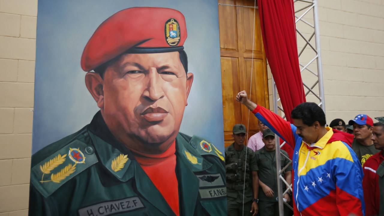 O presidente venezuelano Nicolás Maduro faz uma saudação em frente a um pôster com a imagem de Hugo Chávez. Governo foi criticado em relatório