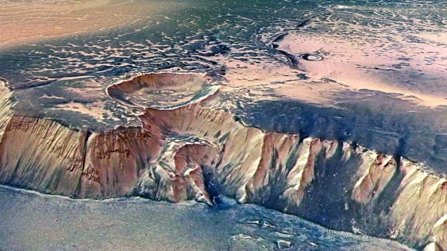 <p>Outro ângulo do gigantesco Echus Chasma, uma das maiores regiões de fonte de água em Marte. Mostra um penhasco impressionante, com 4.000 metros de altura. Cientistas acreditam que cachoeiras colossais já derramaram suas águas através do penhasco há centenas de milhões de anos. O solo, incrivelmente plano, foi inundado por lava basaltica.</p>