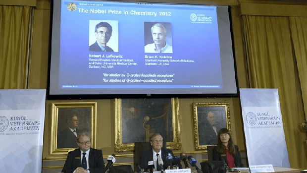 Painel exibe os vencedores do Nobel de Química nesta quarta-feira: os cientistas americanos Robert J. Lefkowitz (à esq. no display) e Brian K. Kobilka (dir.)
