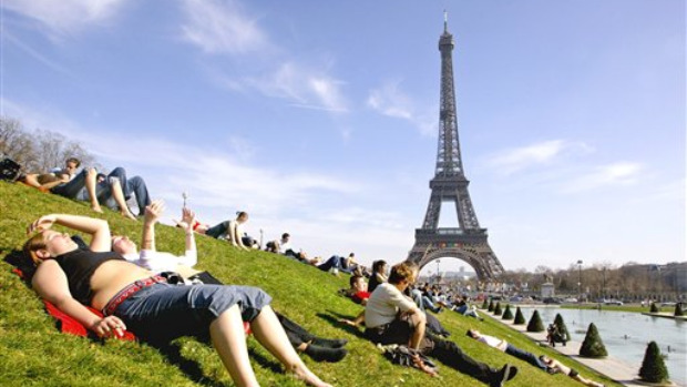Pessoas relaxam ao sol de Paris, tendo a Torre Eiffel ao fundo
