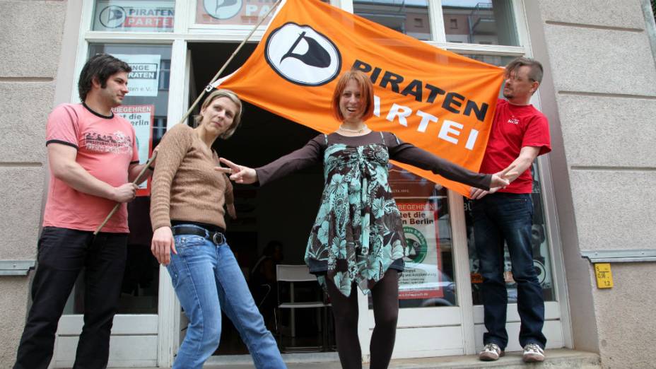 Integrantes do Partido Pirata abrem a bandeira em frente à sede do grupo, em Berlim