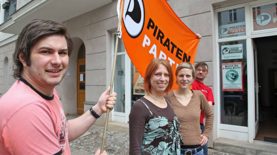 Os piratas alemães agitam a bandeira do grupo, em frente à sede do partido