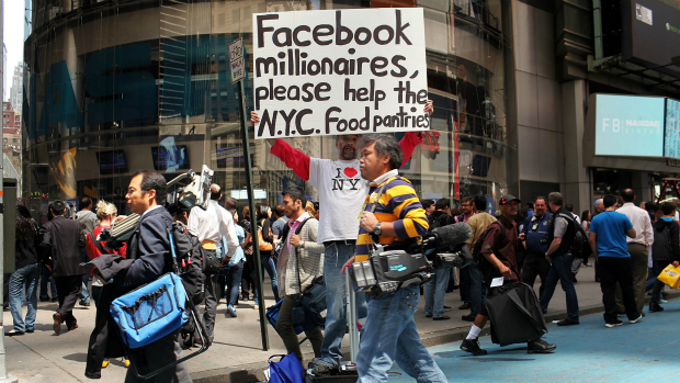 Pedestre segura cartaz em frente à Nasdaq pedindo para que novos milionários do Facebook contribuam na distribuição de alimentos em Nova York
