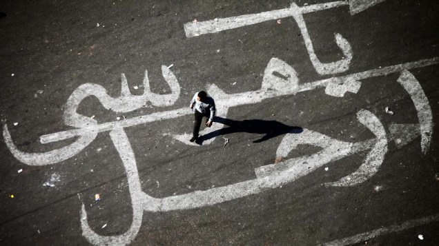 Homem caminha sobre pintura em asfalto com a mensagem Mursi, vá embora, em uma referência ao presidente egípcio, membro da Irmandade Muçulmana