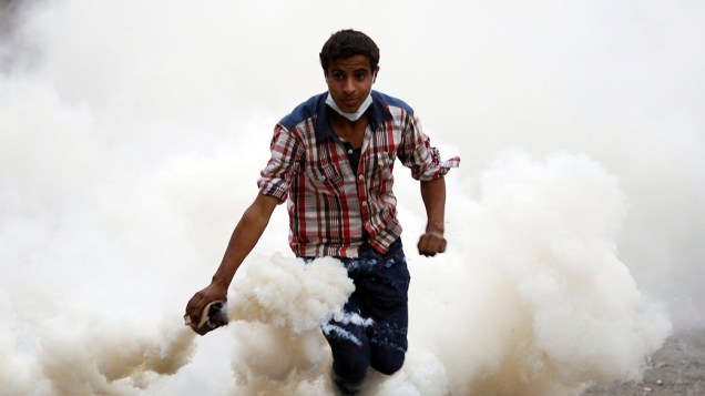 Manifestante joga bomba de gás durante confronto com policiais, próximo da Praça Tahrir