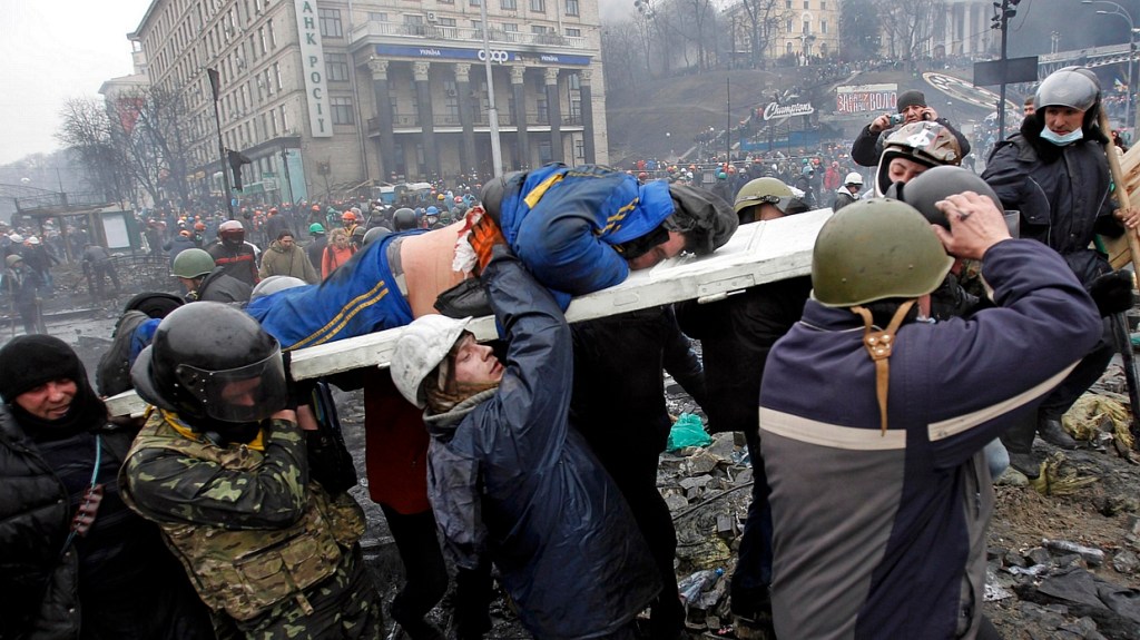 Manifestantes carregam homem baleado na Praça da Independência, em Kiev