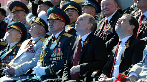 Vladimir Putin, entre primeiro-ministro Dimitri Medvedev (dir.) e o ministro da Defesa, Sergei Shoigu (esq.), assistem ao desfile militar na Praça Vermelha