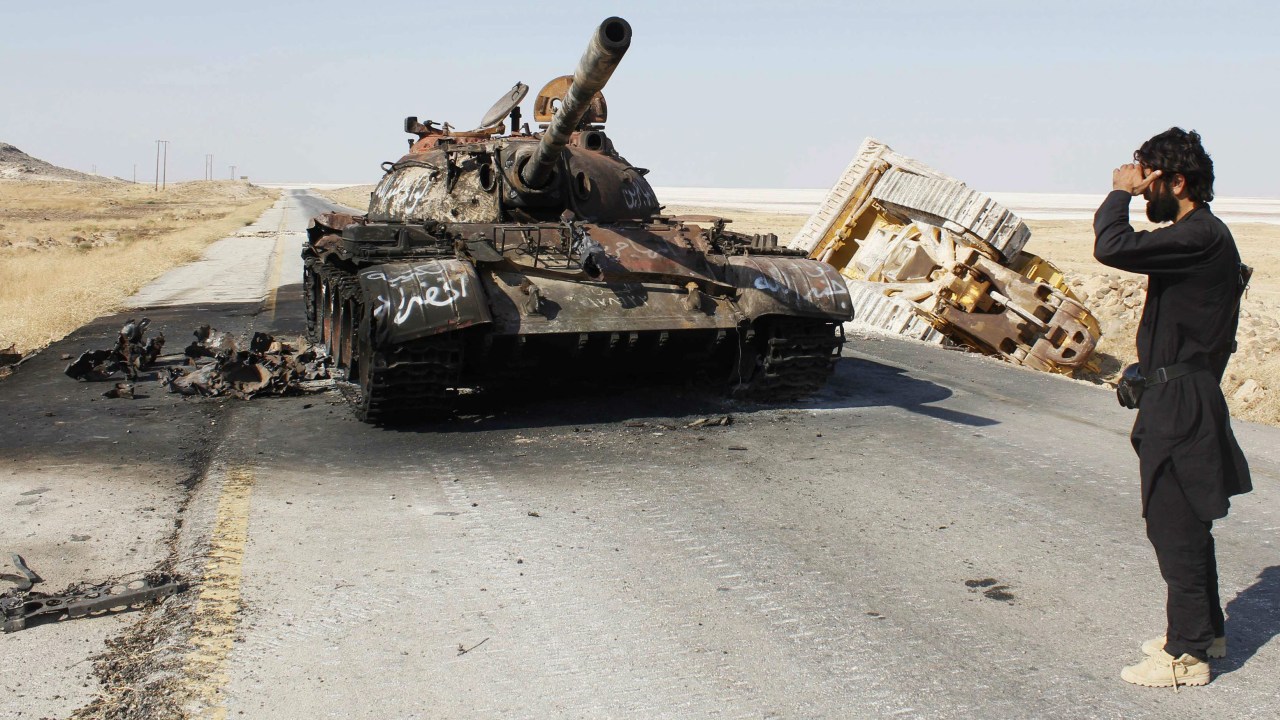 Rebelde sírio observa destroços de tanque que pertencia às tropas de Bashar Assad