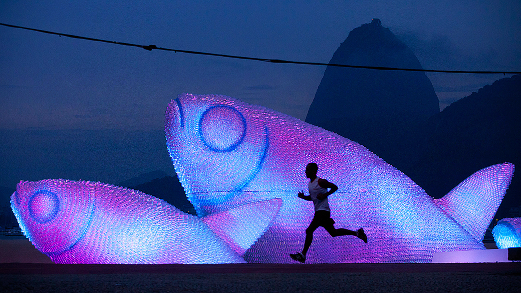 Homem corre próximo a escultura feita de garrafas plásticas na praia de Botafogo, Rio de Janeiro