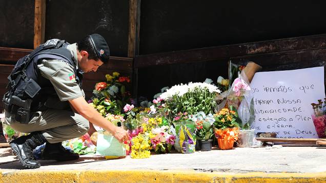 Policial coloca flores em homenagem às vítimas em frente a boate em Santa Maria (RS)