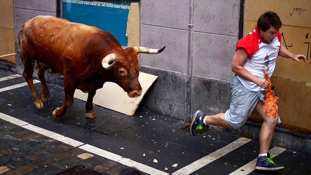 Homem corre de um touro durante o festiva de São Firmino em Pamplona, na Espanha