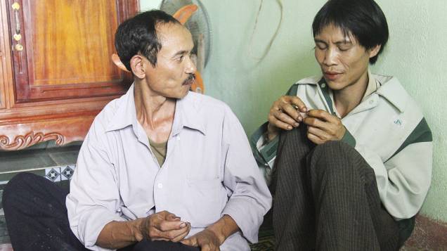 Homem conversa com Ho Van Lang (dir), de 42 anos. Ele passou 40 anos na selva vietnamita sem ter contato com o mundo exterior.