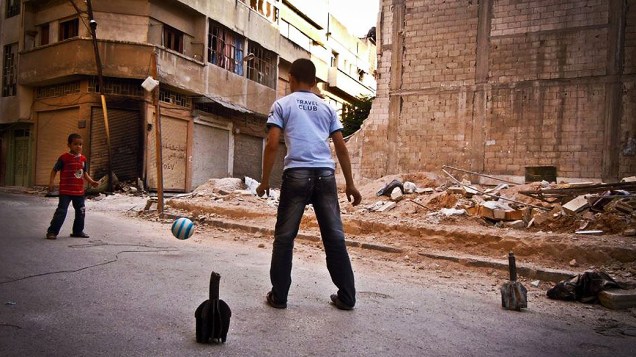 Crianças usam pedaços de morteiros, supostamente disparados por tropas do regime sírio, como goleiras para jogar futebol