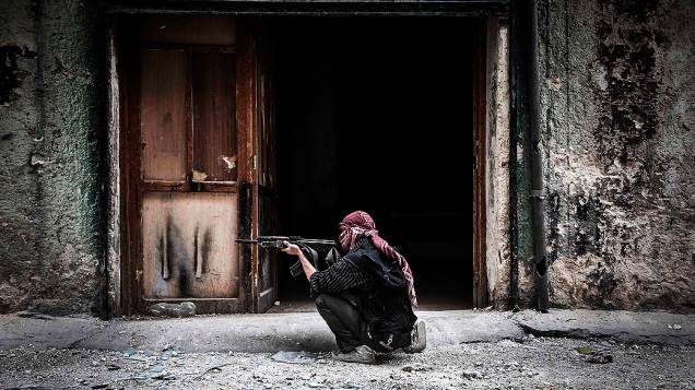 Membro do Exército Livre da Síria dispara contra inimigos na linha de frente de Moaskar, um dos campos de batalha no bairro de Karmal Jabl, em Aleppo