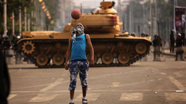 Um apoiador do presidente Mohamed Mursi, joga futebol em frente a tanques do Exército egípcio