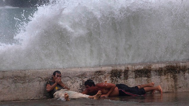 Homens ficam deitados próximo a paredão e observam ondas trazidas pela tempestade tropical Isaac em Baracoa, Cuba