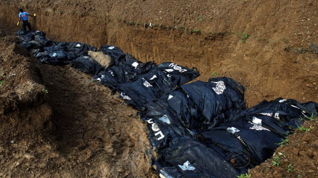 Policial arruma corpos para enterro em uma vala comum, em Tacloban