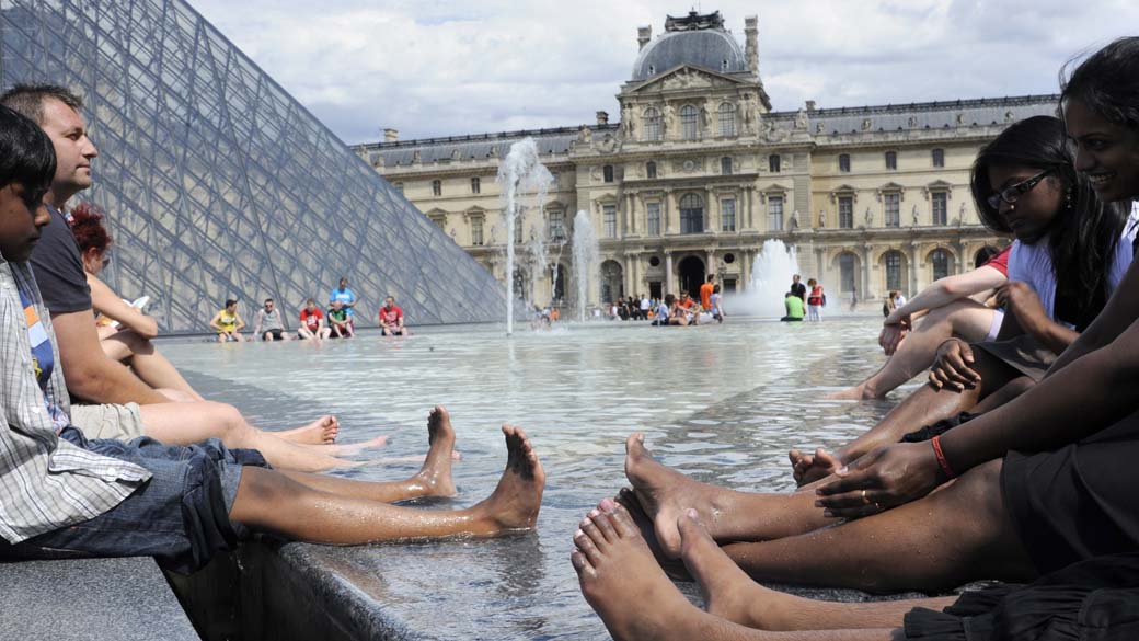 Turistas se refrescam na fonte do Museu do Louvre, em Paris
