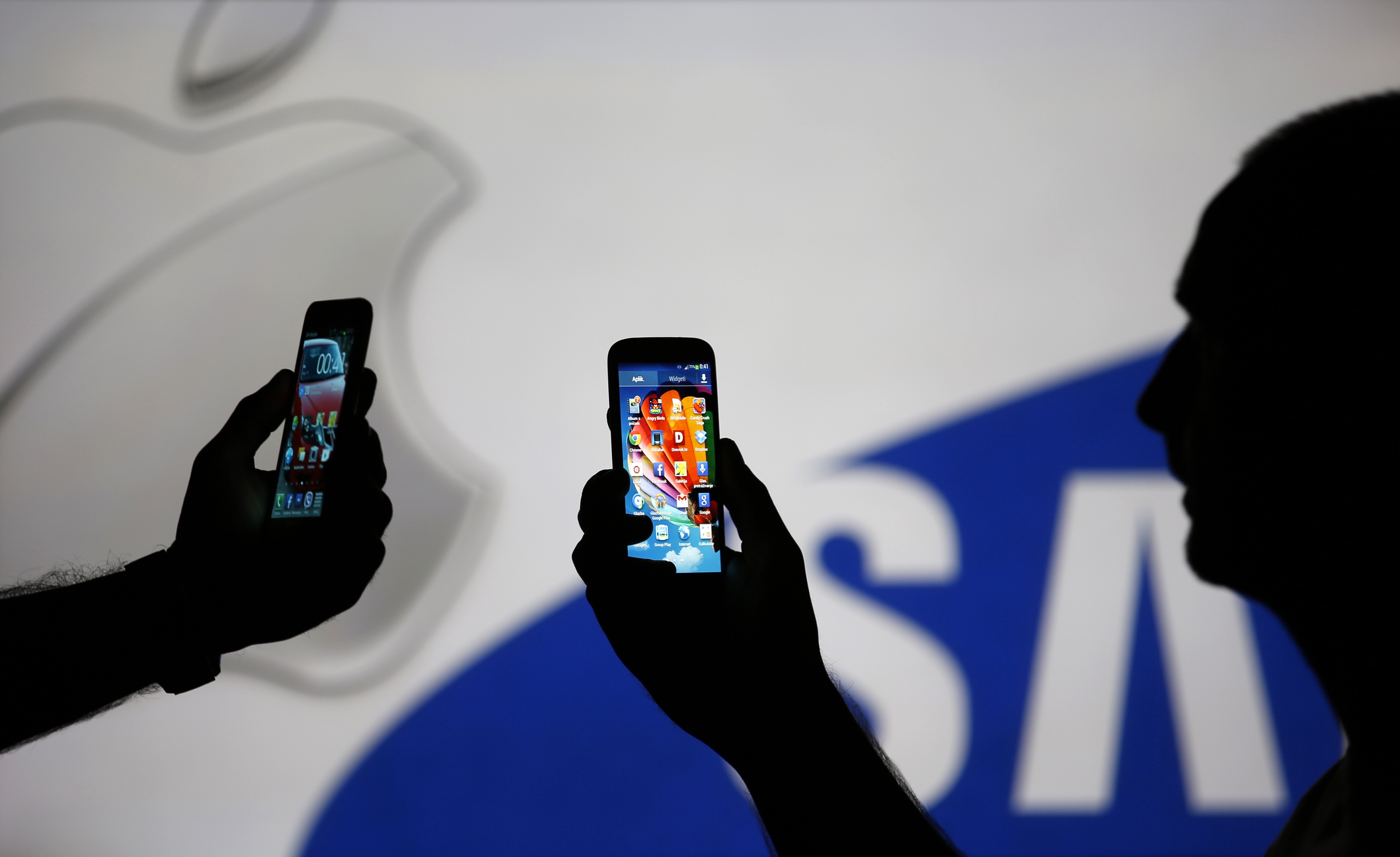 Homens em frente aos logos da Apple e Samsung