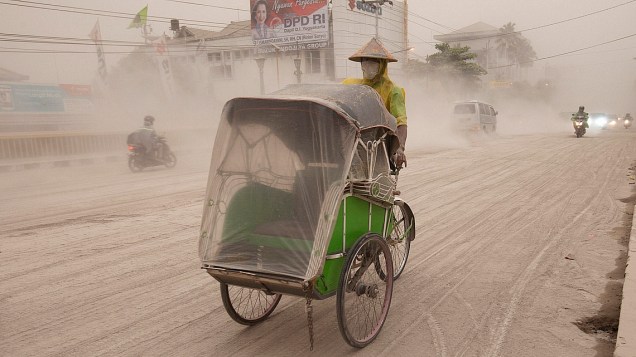Homem dirige um becak, popular meio de transporte na Indonésia, debaixo das cinzas do vulcão